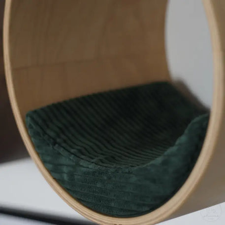 Rundes Holzbett für Haustiere mit grünem Kissen.